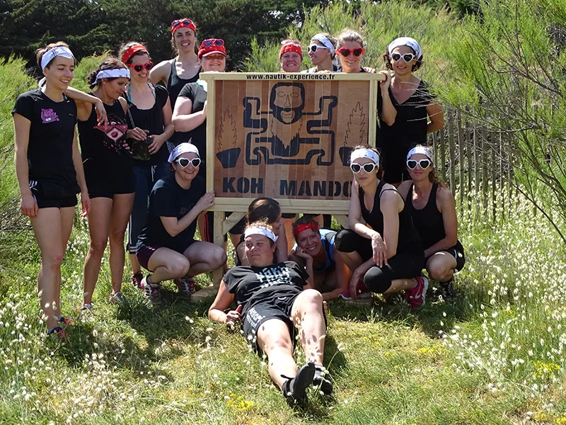 Groupe souriant en tenue de sport rassemblé autour d'un totem en bois lors d'une journée Kib Aventure à Quiberon