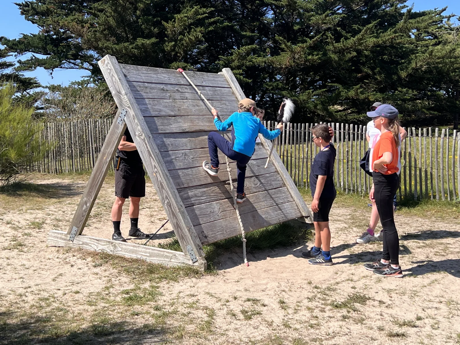 Stage Robinson : enfant grimpant sur un mur incliné en bois avec une corde lors d'un parcours d'obstacles en plein air à Quiberon Bretagne Sud