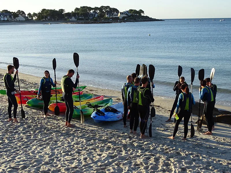 Groupe en combinaisons tenant des pagaies sur la plage aux côtés de kayaks avant une sortie en baie de Quiberon