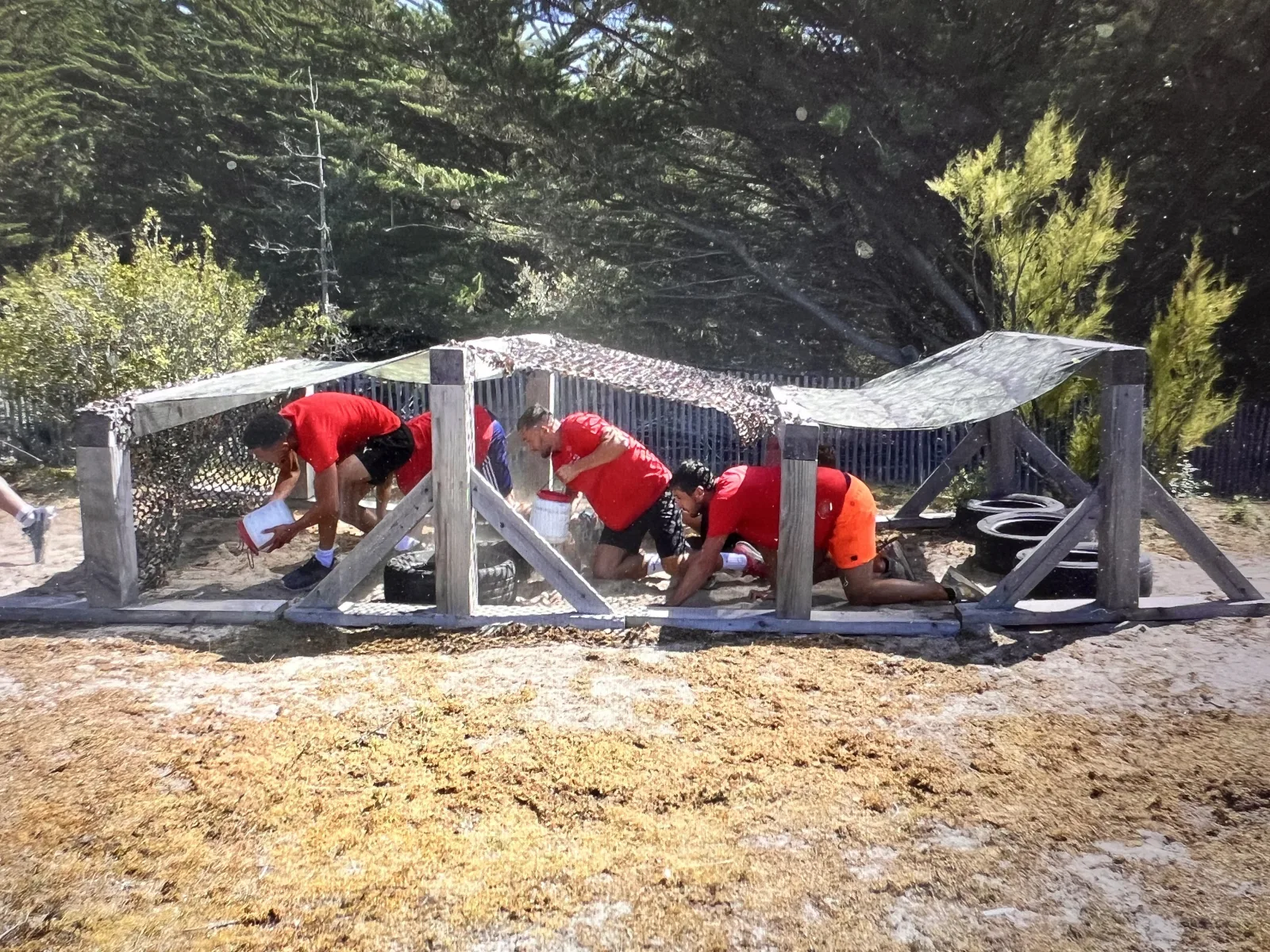 Boot camp : participants en tee-shirts rouges rampant sous des filets de camouflage lors d'un parcours du combattant à Quiberon Bretagne Sud