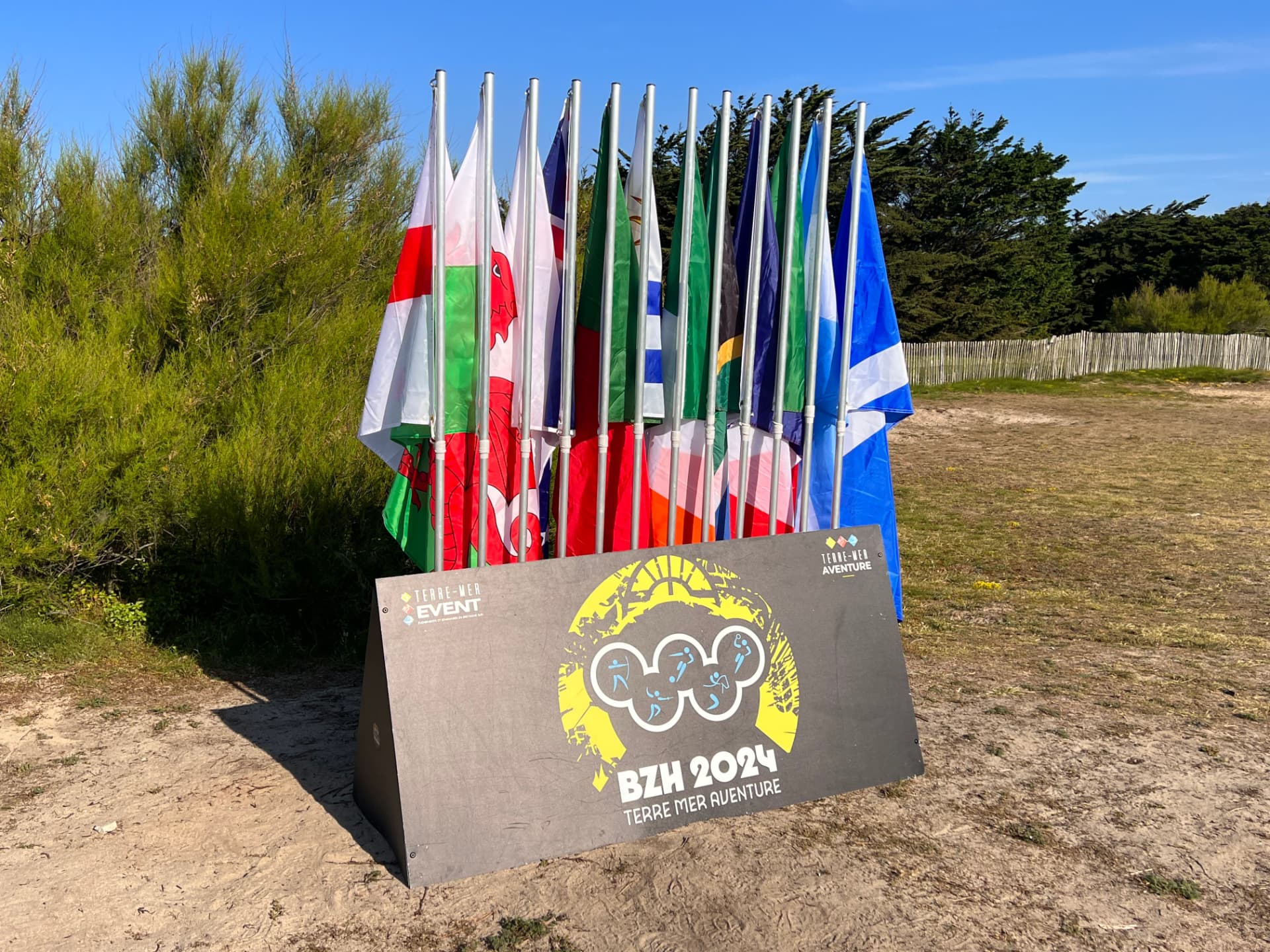 Panneau BZH 2024 Terre-Mer Aventure avec anneaux olympiques et drapeaux nationaux, compétition d'Olympiades en Bretagne