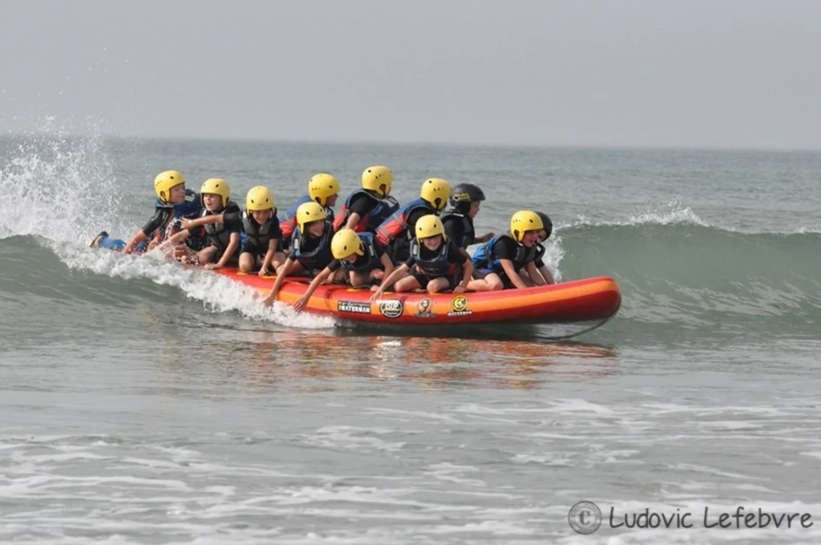 Groupe d'enfants surfant une vague sur un paddle géant, raft de mer Bretagne Sud
